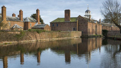 A view of the moat with Dunham Massey house, coach-house, and stables reflected in the water, Cheshire.